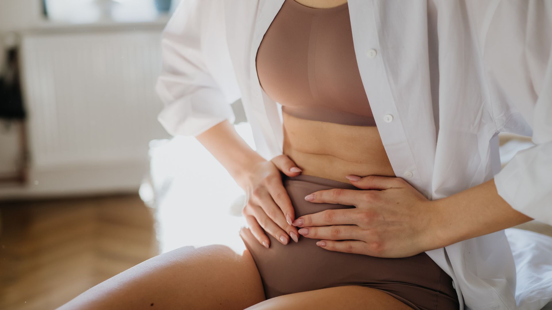 A woman sitting on a bed with her stomach exposed